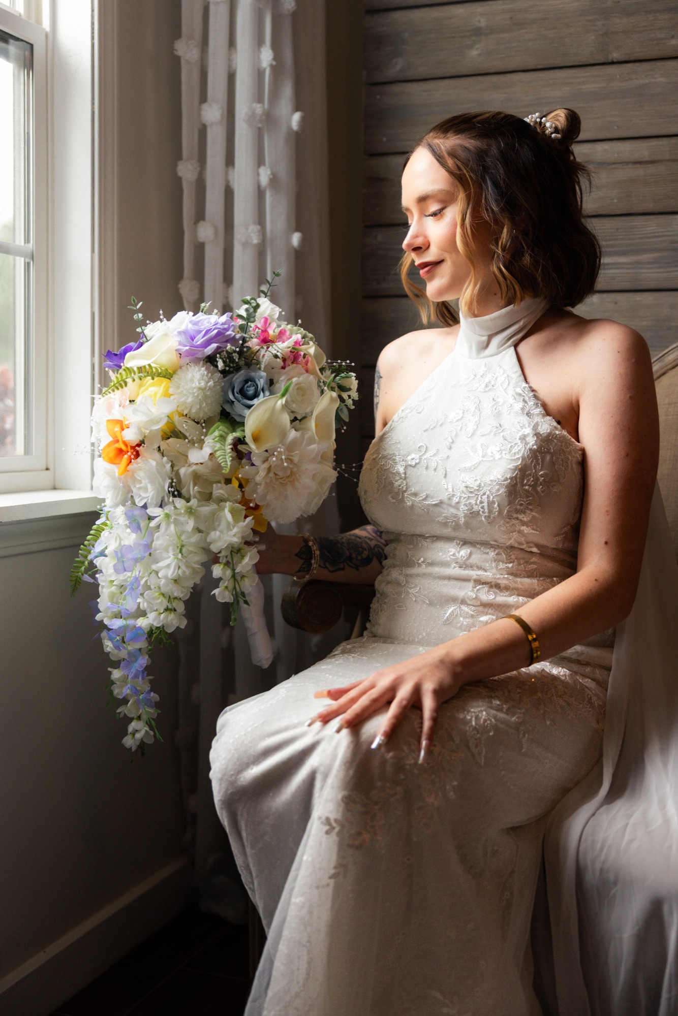 Bride seated beside a window holding a cascading bouquet