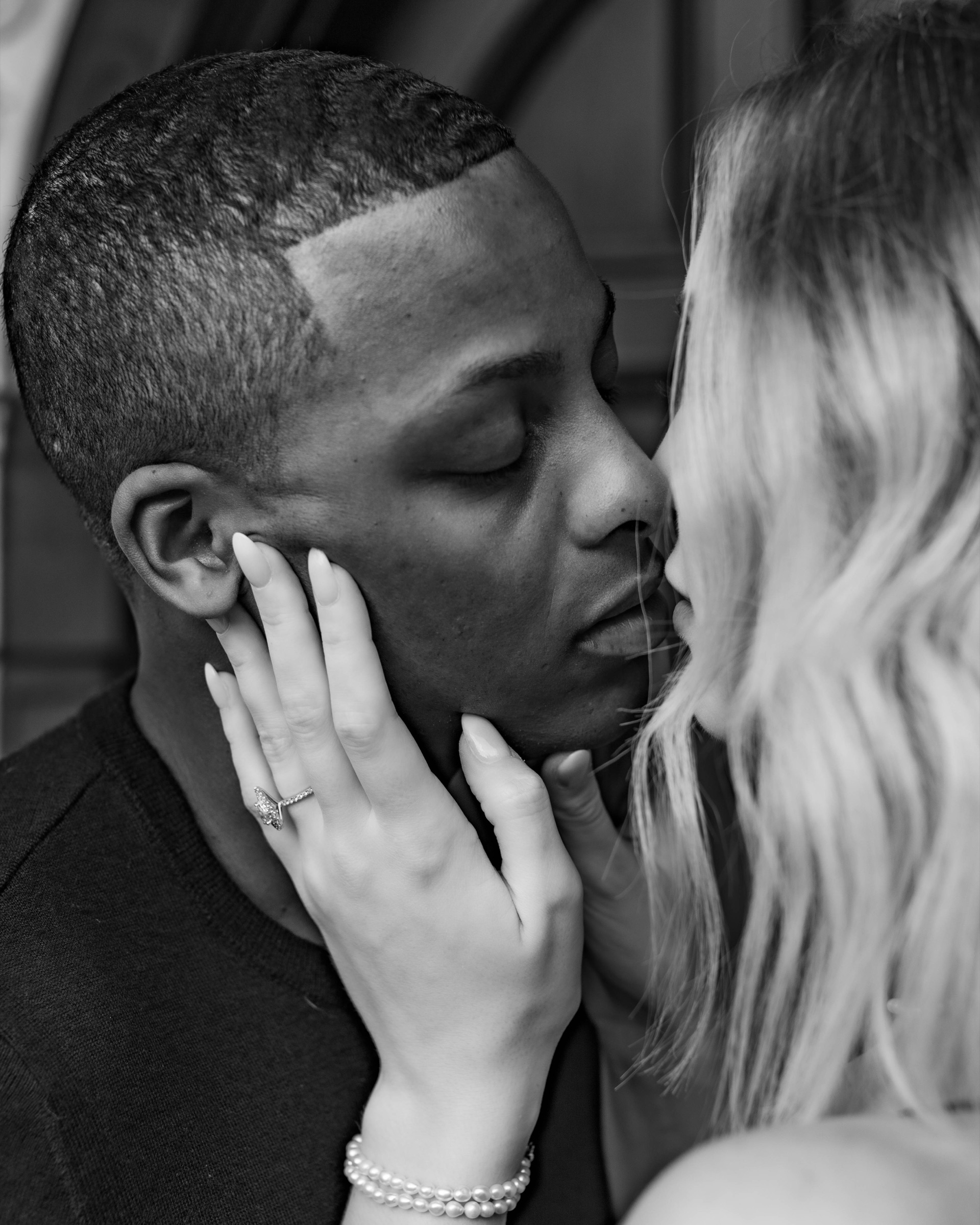 Engaged couple sharing a close black and white kiss with the ring in view