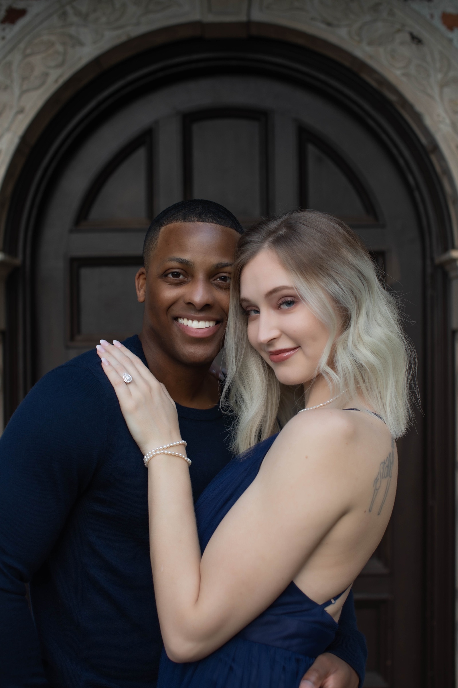 Engaged couple smiling together in front of an arched wooden doorway