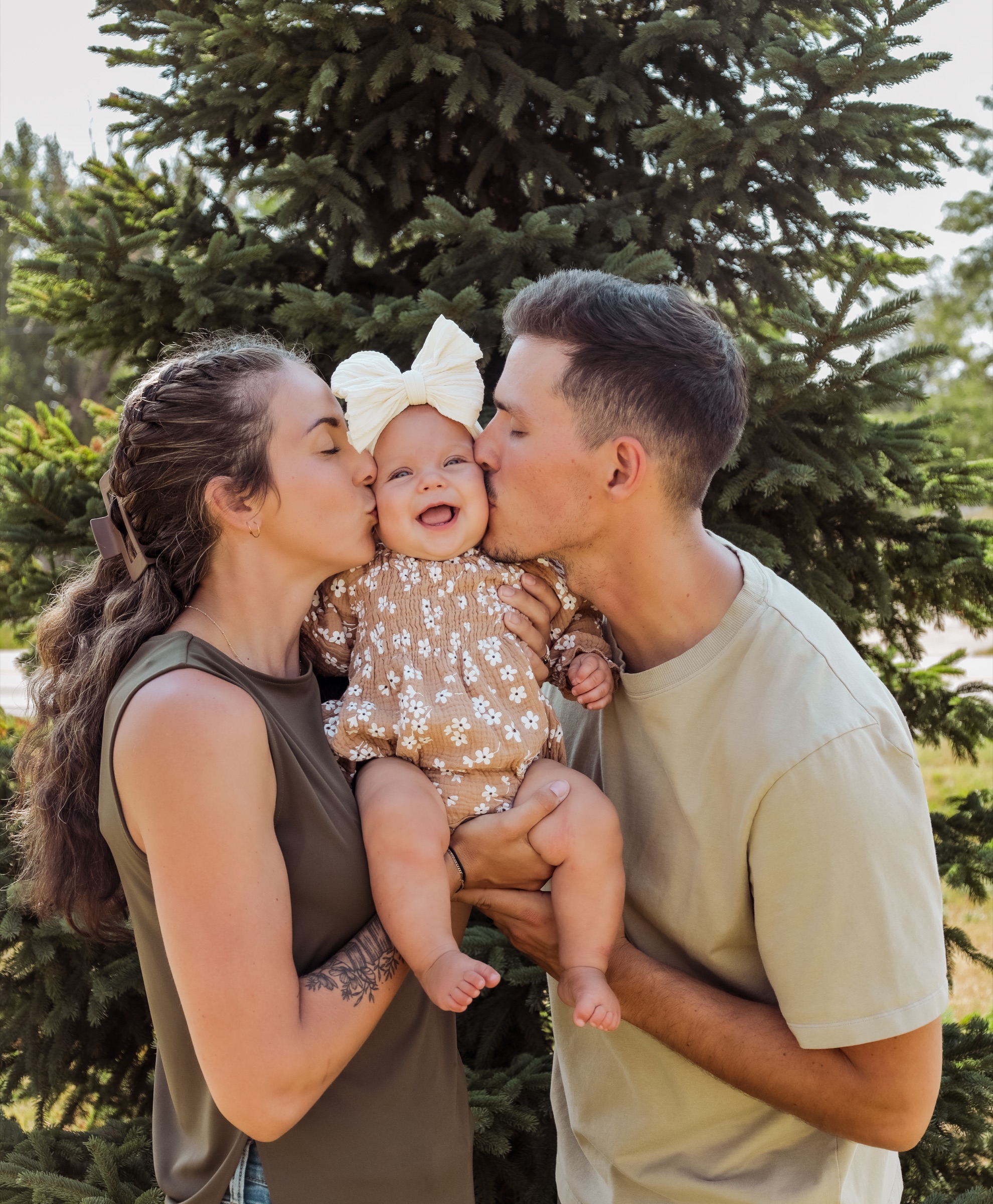 Parents kissing the cheeks of their smiling baby outdoors