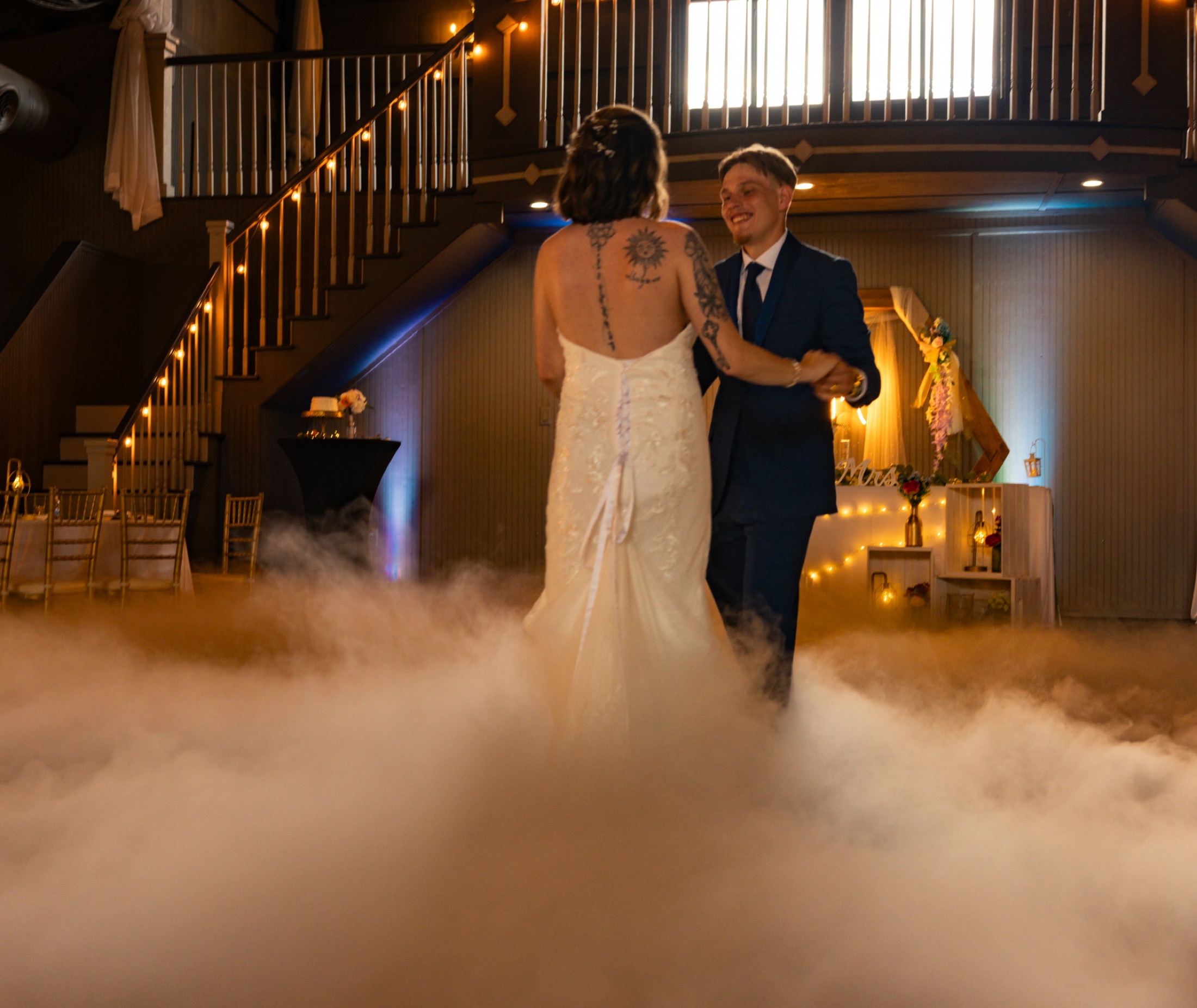 A couple sharing their first dance in a room filled with fog and warm lights
