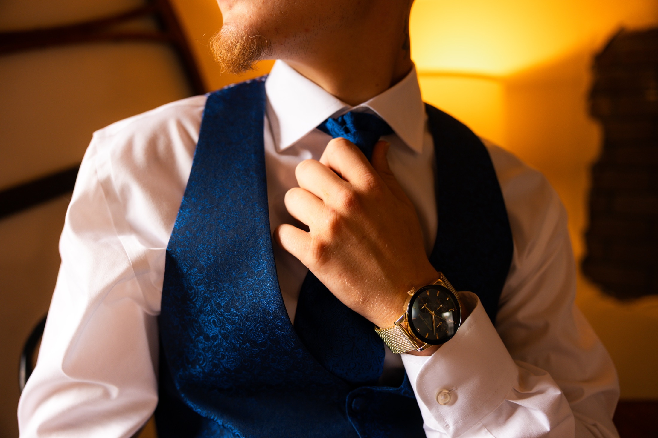 Groom adjusting his tie in warm window light