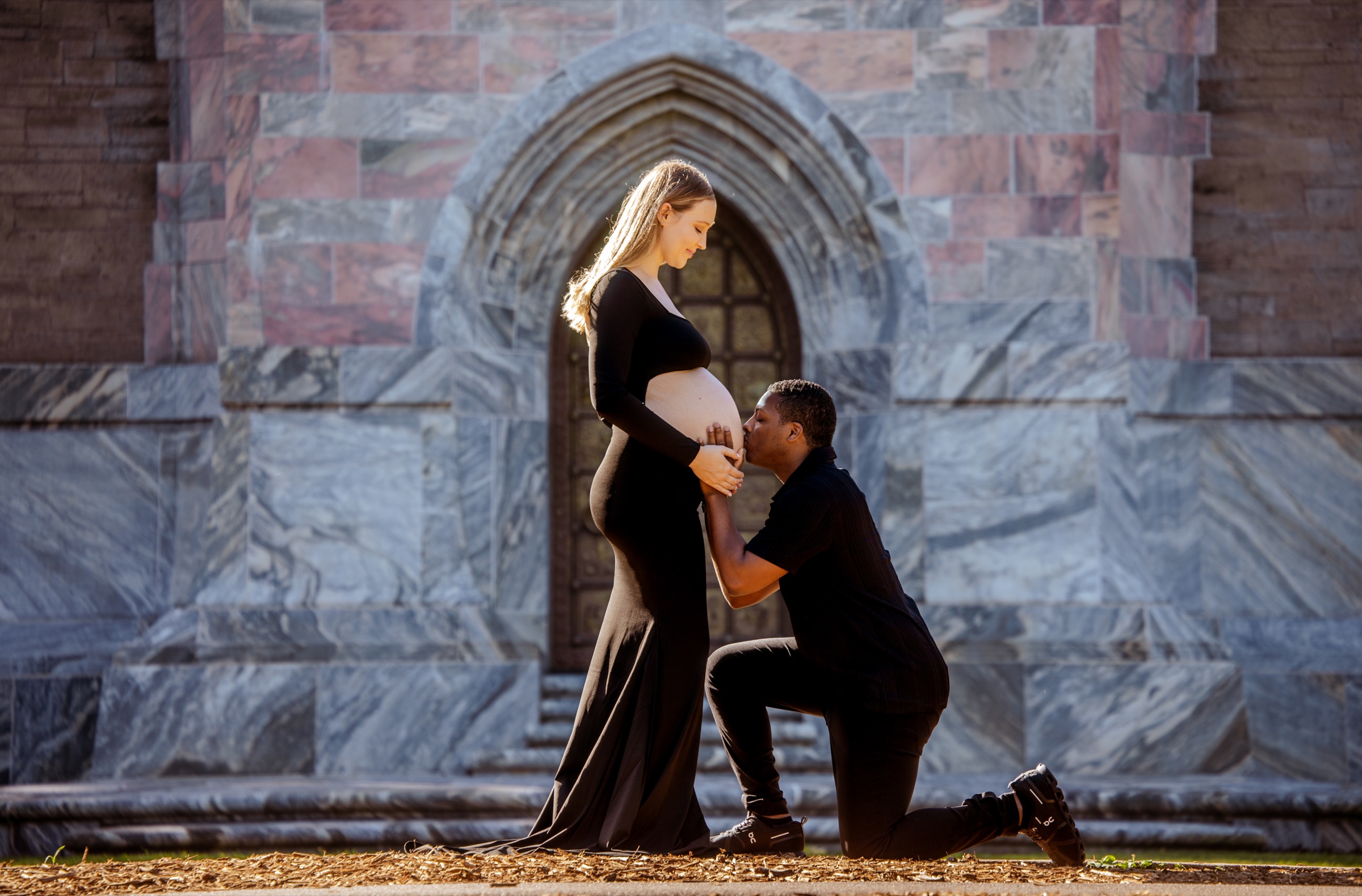 Expecting couple sharing a tender moment in front of an arched stone doorway