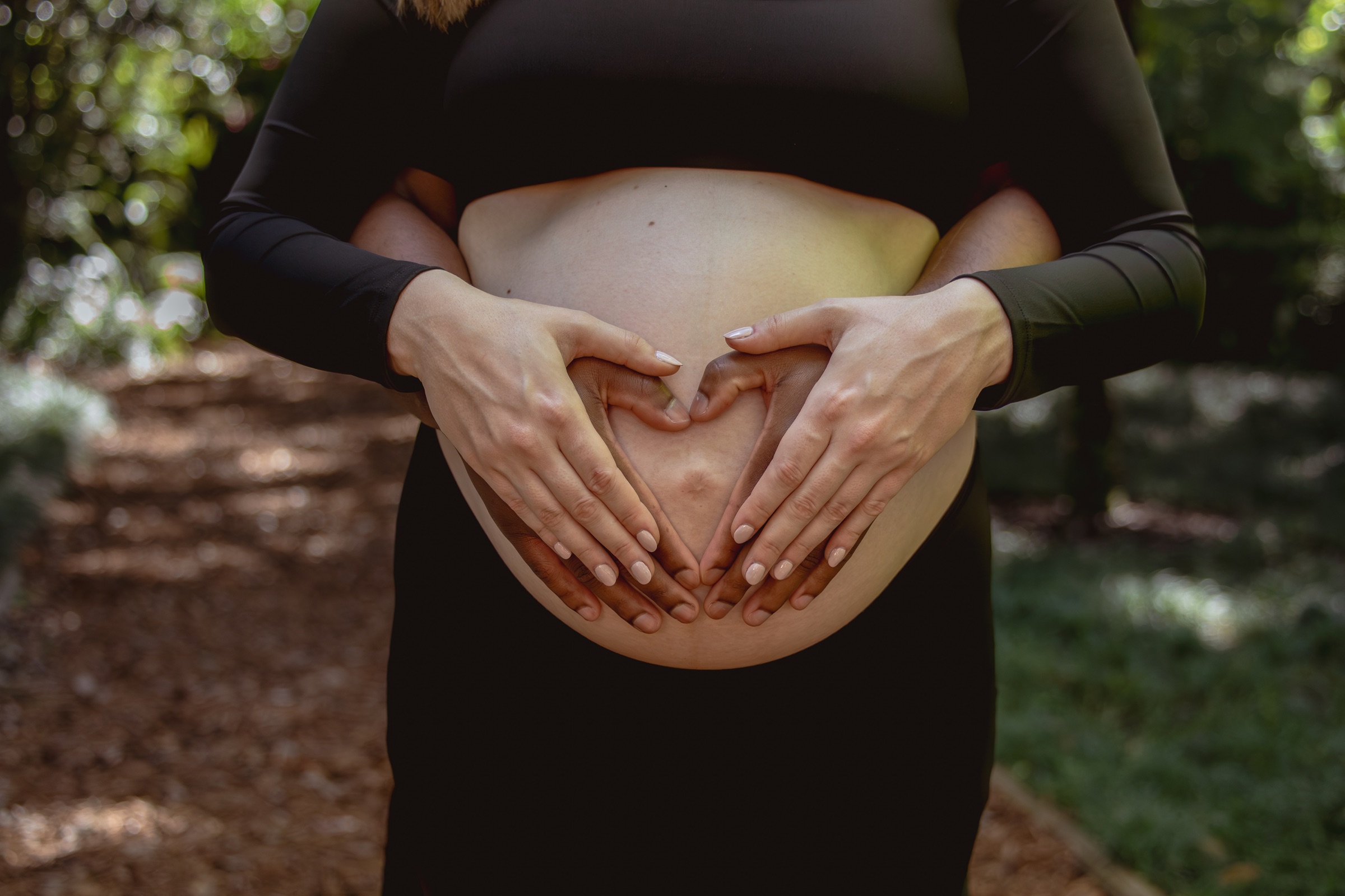 Expecting parents making a heart with their hands over a baby bump